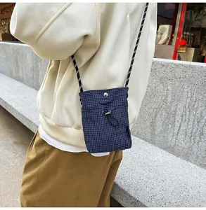 Dettaglio di una mini borsa a tracolla a quadretti blu scuro indossata sopra una felpa.
