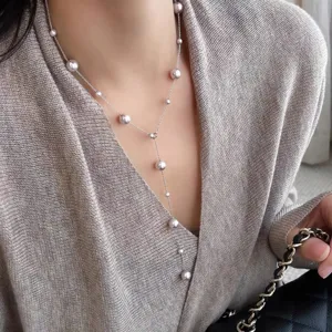Elegant Y-shaped long necklace with multi-sized pearls worn over a grey sweater detail.
