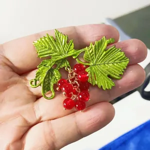Close-up of a vintage baroque grape brooch with green leaves and red beads held in hand.