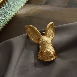 Detailopname van een vintage matgouden konijnenkopbroche op grijze zijde.