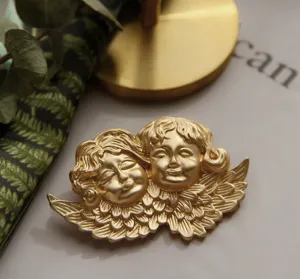 Gedetailleerd beeld van een vintage matgouden broche met twee cherubijnen en vleugels.