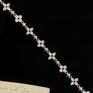 Detail view of silver-toned bracelet with clover motifs and zircon stones on black background.