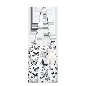 Detailed view of white canvas tote bag featuring black butterfly prints and a bear charm