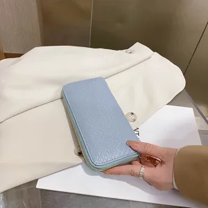 Macro view of a light blue crocodile pattern wallet held in hand, showing fine texture.