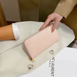 Macro detail of elegant pink crocodile textured long wallet held over white blazer garment