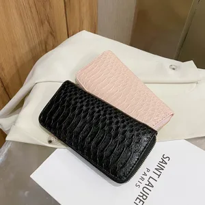 High-angle view of black and pink crocodile embossed long wallets on white fabric.