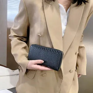 Black crocodile pattern long wallet clutch held by a woman in a beige blazer