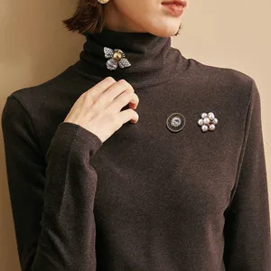 Detailed view of three vintage Baroque brooches worn on a dark brown turtleneck sweater
