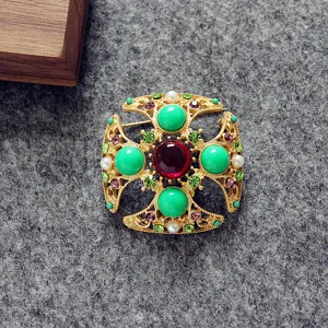 Primer plano de un broche barroco cuadrado con piedras verdes y rojas vibrantes