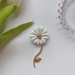 Primo piano di un'elegante spilla a margherita bianca con stelo e foglia dorati