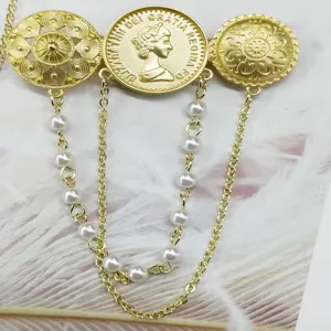 Dettaglio di una spilla vintage dorata con rilievo della regina e nappe di perle