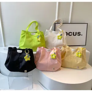 Vista detallada de los bolsos tote de lona colorida con dijes de flores y etiquetas.