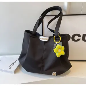 Primer plano del bolso tote de lona negra con colgante de flor amarilla y asas prácticas.
