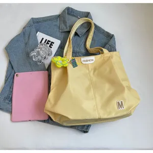 Vista detallada del bolso tote amarillo de lona con una etiqueta de moda y parche M.