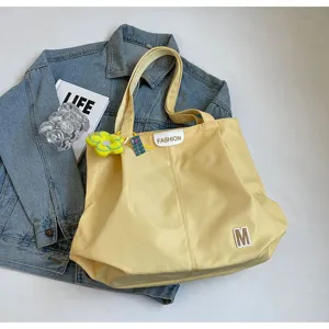 Detalle de bolso tote de lona amarilla, con parche letra M y etiqueta fashion, estilo casual.
