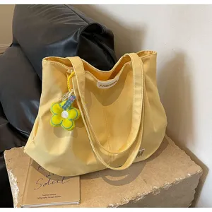 Vista detallada del bolso tote de lona amarilla con etiqueta frontal, colgante de flor y textura.