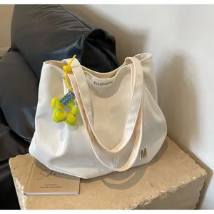 Vista detallada de un elegante bolso shopper de lona blanca con colgante floral amarillo y parche.