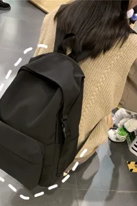 Back view of a minimalist black nylon rucksack worn over a beige sweater for school