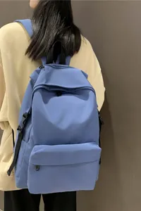 Back view of a minimalist blue waterproof nylon student backpack on a casual outfit.