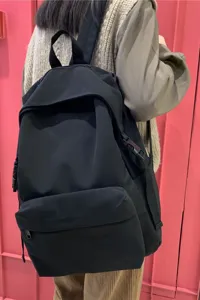 Detailed back view of a minimalist black nylon student backpack on a model.