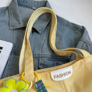 Detalle de bolso tote de lona amarilla, con parche de moda y linda decoración de flores.