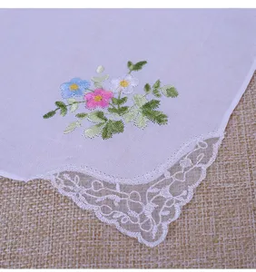 Gros plan d'un mouchoir en coton blanc avec broderie florale et fine bordure en dentelle.