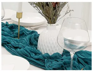 Runner da tavola in garza blu petrolio con trama stropicciata naturale su tavola bianca