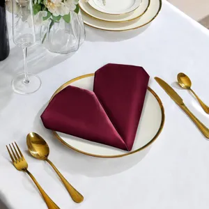 Burgundy satin dinner napkin folded in heart shape for elegant hotel table decoration and events.