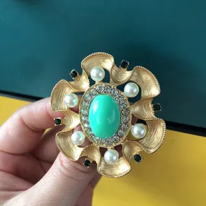 Vintage Baroque style gold brooch featuring a large green stone and pearls, hand held view