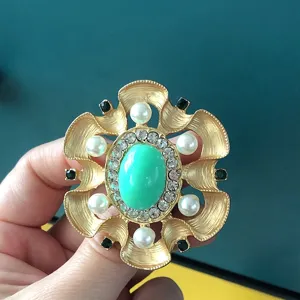 Close-up of vintage baroque brooch with green stone, pearls and rhinestones detail