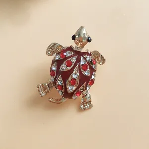 Detailed shot of a gold-tone turtle brooch with red and white rhinestones and enamel finish.