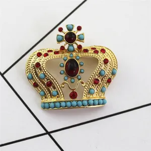 Detalle de broche de corona dorado vintage con pedrería roja y cuentas de turquesa.