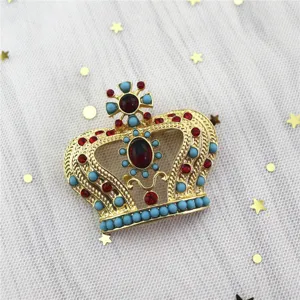 Primer plano detallado de un broche de corona de oro vintage con piedras rojas y azules