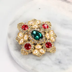 Vista detallada de un broche barroco vintage con piedras preciosas verde esmeralda y rojo.