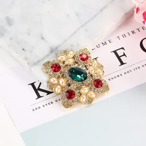 Detalle de un broche barroco vintage con gema verde esmeralda, cristales rojos y perlas