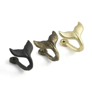 Close-up of three vintage cast iron whale tail wall hooks in black, bronze, and gold.