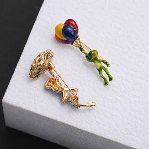 Close-up view of a green enamel frog brooch holding colorful balloons with back pin detail