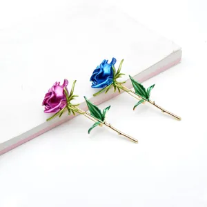 Zwei elegante Rosenbroschen mit pinkfarbenem und blauem Emaille-Finish auf einem Buch
