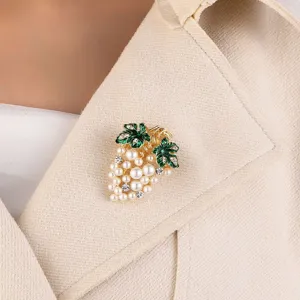 Close-up of elegant grape brooch with pearls and green leaves on a beige coat
