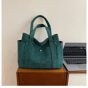Dettaglio lifestyle di borsa tote in velluto a coste verde scuro su scrivania in legno
