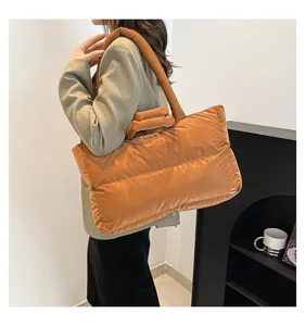 Large caramel colored padded puffer tote bag shown on model in a minimalist studio.