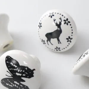 Close-up macro view of white ceramic drawer knobs with black deer and butterfly designs.