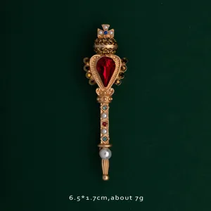 Detailed view of an ornate gold wand brooch with a vibrant red heart gemstone.