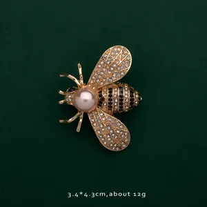 Macro view of a gold bee brooch featuring sparkling rhinestones and a large pearl.