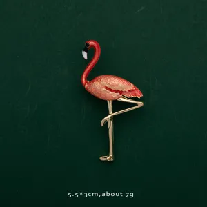 Close-up of elegant red flamingo brooch pin with gold-plated legs on green background