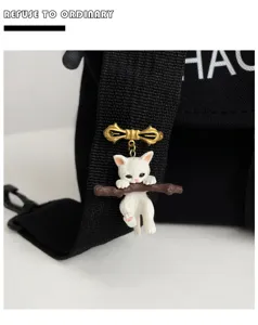 Close-up of a cute 3D white kitten holding a branch brooch attached to a black bag strap.