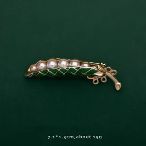Close-up view of a vintage pea pod brooch featuring white pearls and green enamel