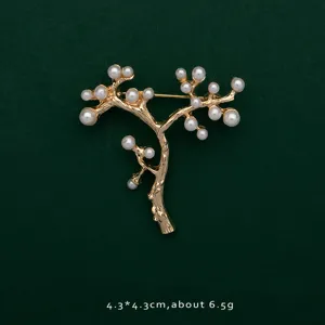 Close-up of gold-plated tree branch brooch with elegant white pearls on green background.