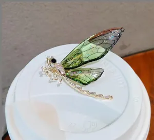 Detailed close-up of a luxury gold and green dragonfly brooch with shimmering wings.