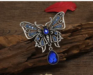 Vintage hollow butterfly brooch with blue rhinestones and water-drop pendant on wood.